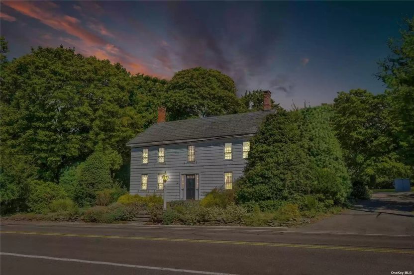 Lighted exterior of 1750 home at dusk in Stony Brook, NY