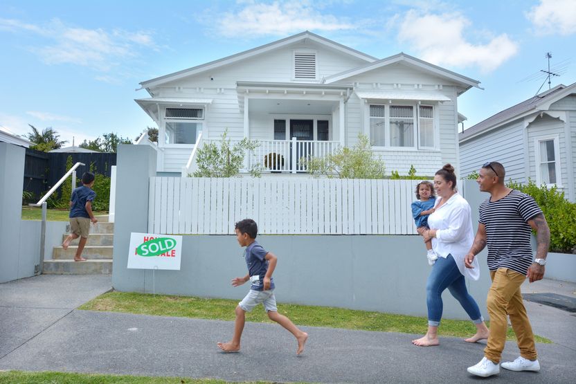 Happy Maori family walking towards their new home with a sold sign on traditional bungalow house in