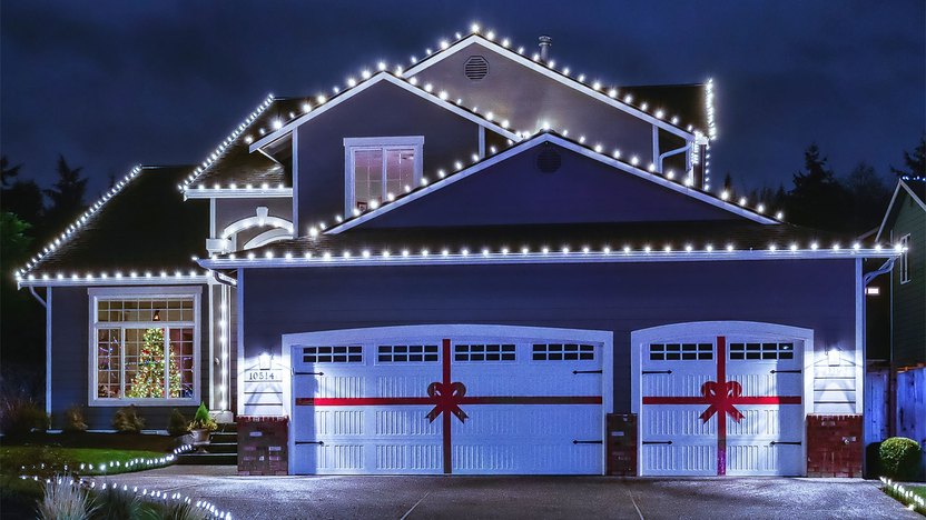 Night time photo of a modern American suburban home decorated with festive Christmas holiday lights and red ribbons on garage doors